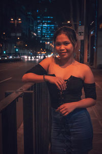 Smiling young woman standing against illuminated city at night