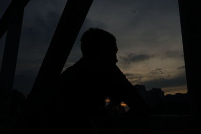 Silhouette man looking through window at sunset