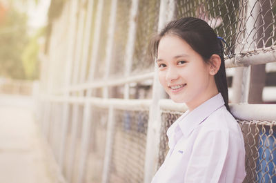 Portrait of smiling young woman standing by fence