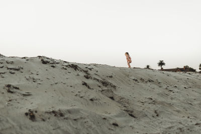 Wide view of toddler girl walking in sand at beach