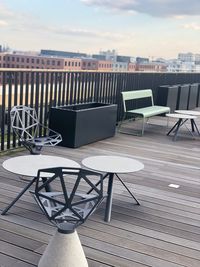 Empty chairs and tables by railing against sky