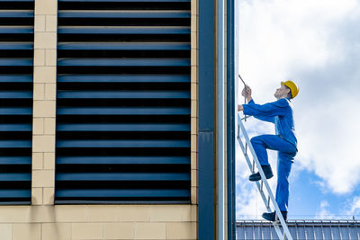 Full length side view of manual worker cleaning building while standing on ladder