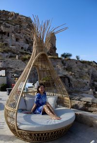 Portrait of happy woman sitting on bamboo sun lounger against blue sky