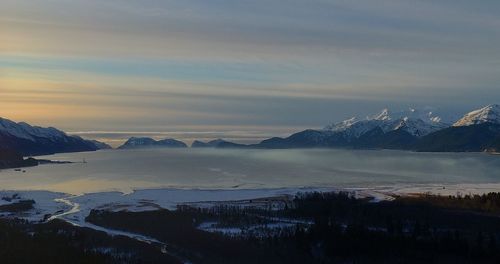 Scenic view of lake by snowcapped mountains against sky during sunset