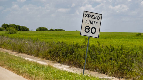 Information sign on road by field against sky