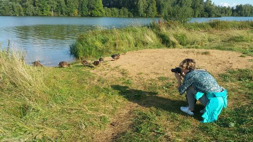 Rear view of woman sitting on grass by lake