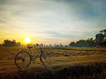 Bicycle parked on grassy field against sky during sunset