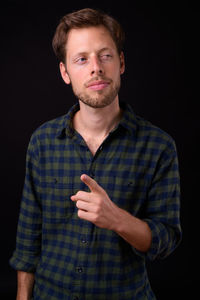 Portrait of young man standing against black background