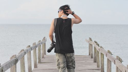 Man standing on railing by sea against sky