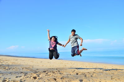 Full length of men jumping on beach against sky