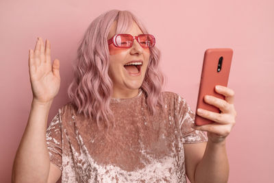 Portrait of young woman using mobile phone against wall