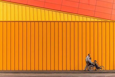 Side view of man sitting against orange wall