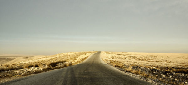 Empty road amidst field against sky