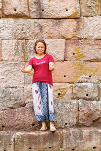 Portrait of woman gesturing against stone wall