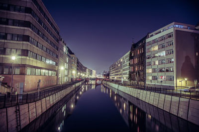 Canal amidst illuminated buildings at night