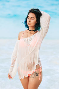 Portrait of beautiful young woman standing at beach against sky