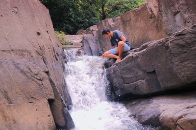 Rear view of young woman standing on cliff by waterfall