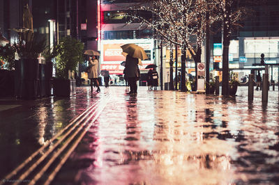 Full length of woman standing on wet sidewalk in city during rainy season