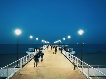 People walking on illuminated beach against clear sky