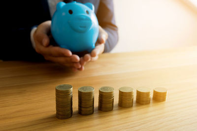 Close-up of coins with man holding piggy bank on table