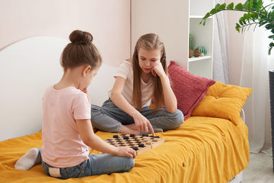 Sisters playing draughts board game on bed