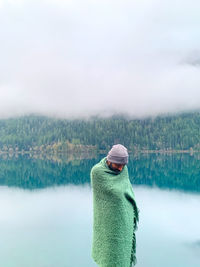 Man wrapped in blanket standing against lake during winter