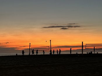 Silhouette people on beach against sky during sunset