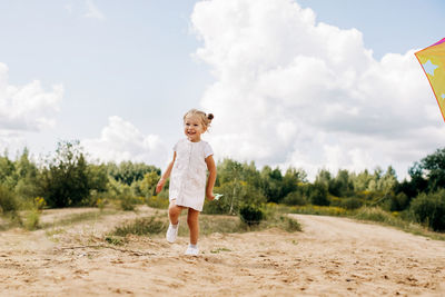 A little girl is flying a kite on a field road outside the city. childhood, joy, care