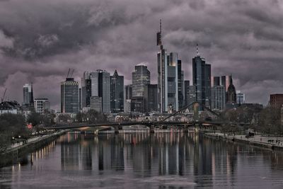 Bridge over river by buildings against sky in city