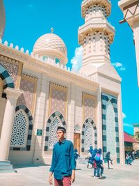 Man standing outside mosque against blue sky