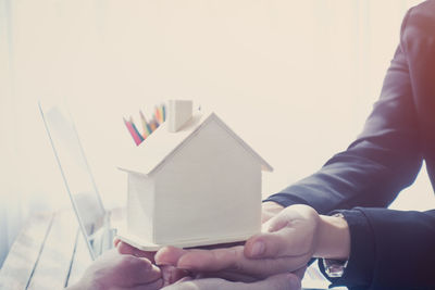 Close-up of salesman holding model home by laptop at table