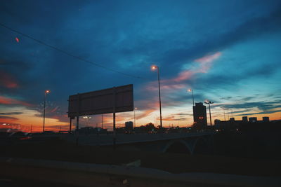 Road by silhouette city against sky at sunset