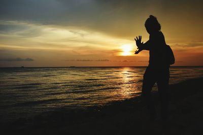 Silhouette woman standing on beach against orange sky