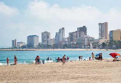 People at beach in city against cloudy sky