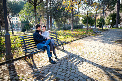 The young couple is sitting on a bench in the park in rome. 