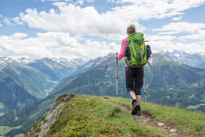 Rear view of man standing on mountain against cloudy sky