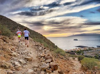 Rear view of people standing on shore against sky