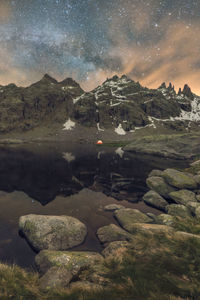 Scenic view of distant tent on lake shore against snowy mountain under cloudy sky in evening