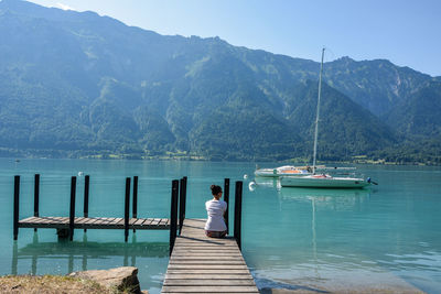 Rear view of woman sitting on pier over lake against mountains