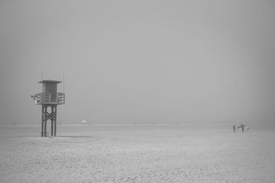 Fog over the beach with surfers walking on the sand