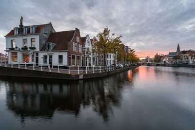 Canal by houses in town against cloudy sky