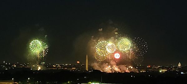 Firework display over illuminated city against sky at night