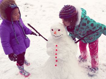 High angle view of sisters playing with snowman