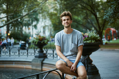 Portrait of young man sitting by fountain at park