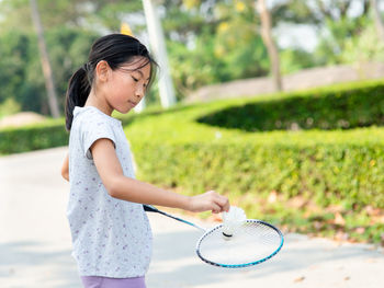 Side view of girl playing badminton while standing on footpath 
