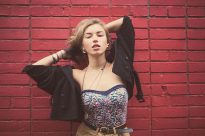 Portrait of young woman standing against brick wall