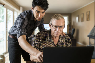 Grandson assisting grandfather in using laptop at home