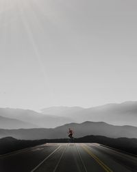 Distant view of man jumping over road amidst mountains against sky