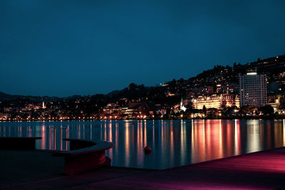 Illuminated buildings by sea against sky at night