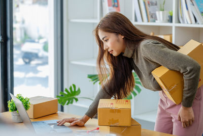 Portrait of young woman using laptop while standing by window at home